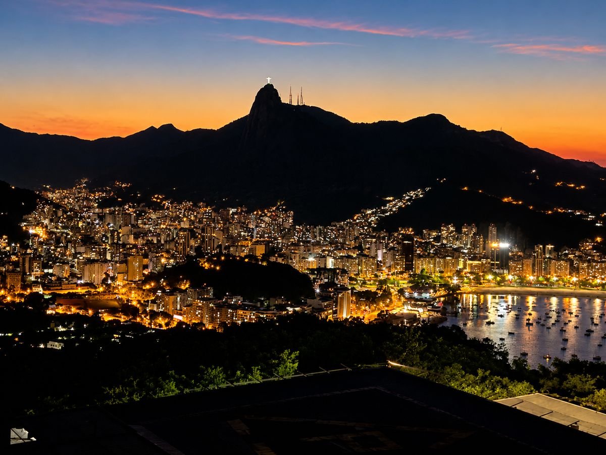 Christ the Redeemer silhouetted above Rio at dusk, the city lights glowing below